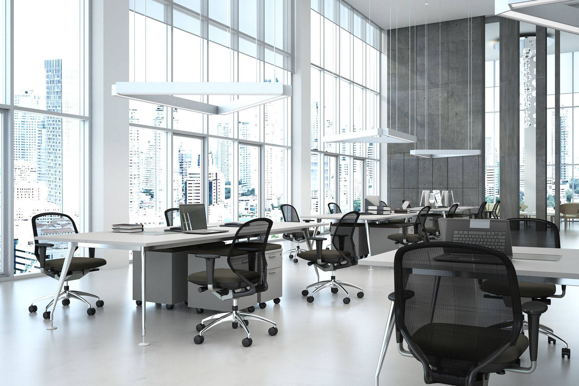 A spacious modern office with large windows offering a view of city buildings. Several workstations with black mesh chairs, white desks, and computer monitors are arranged throughout the room. The office features bright lighting, a minimalistic design, and benefits from professional cleaning services.