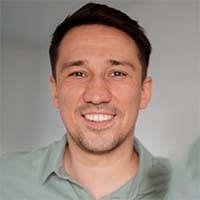 A man with short dark hair is smiling at the camera. He is wearing a light green shirt and standing against a gray background, looking like he just finished some height cleaning.