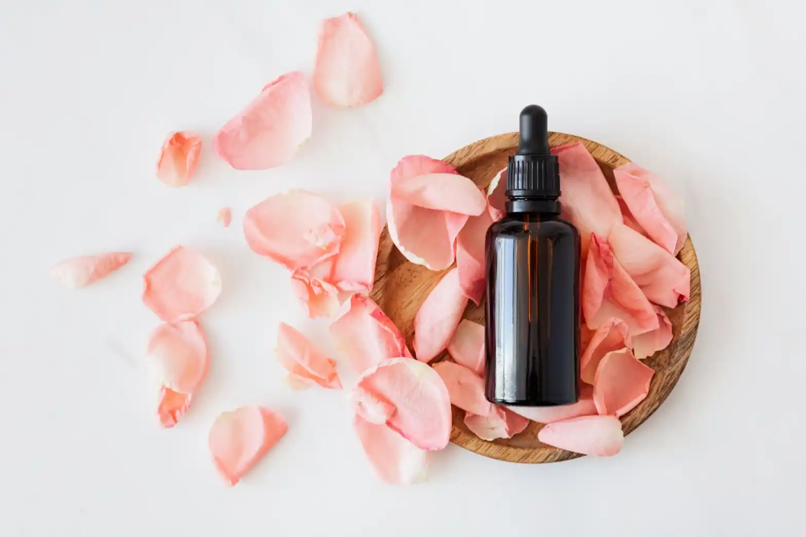 a brown bottle of essential oil on a basket with pink petals